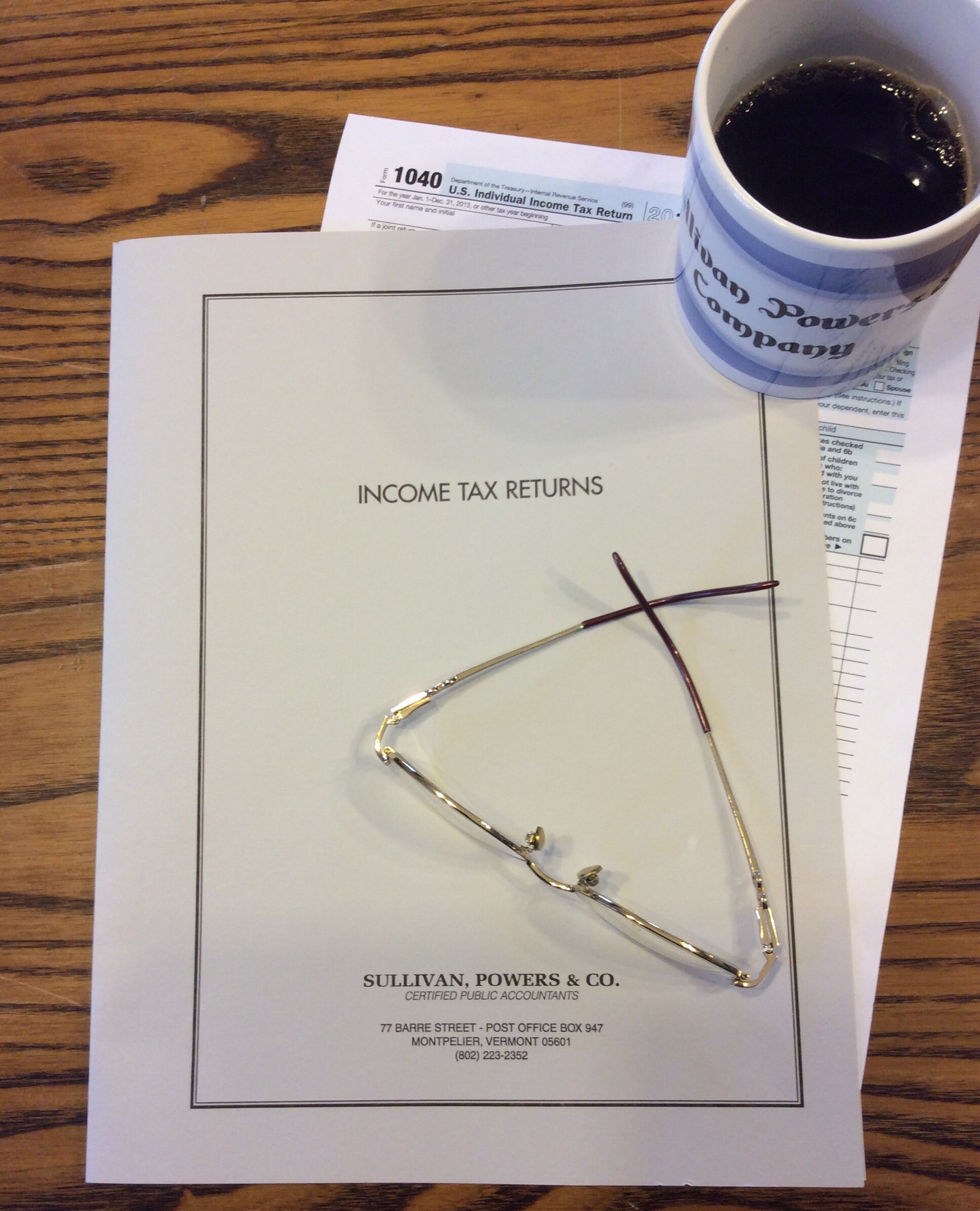 Tax documents, glasses, and a coffee mug on a wooden table.