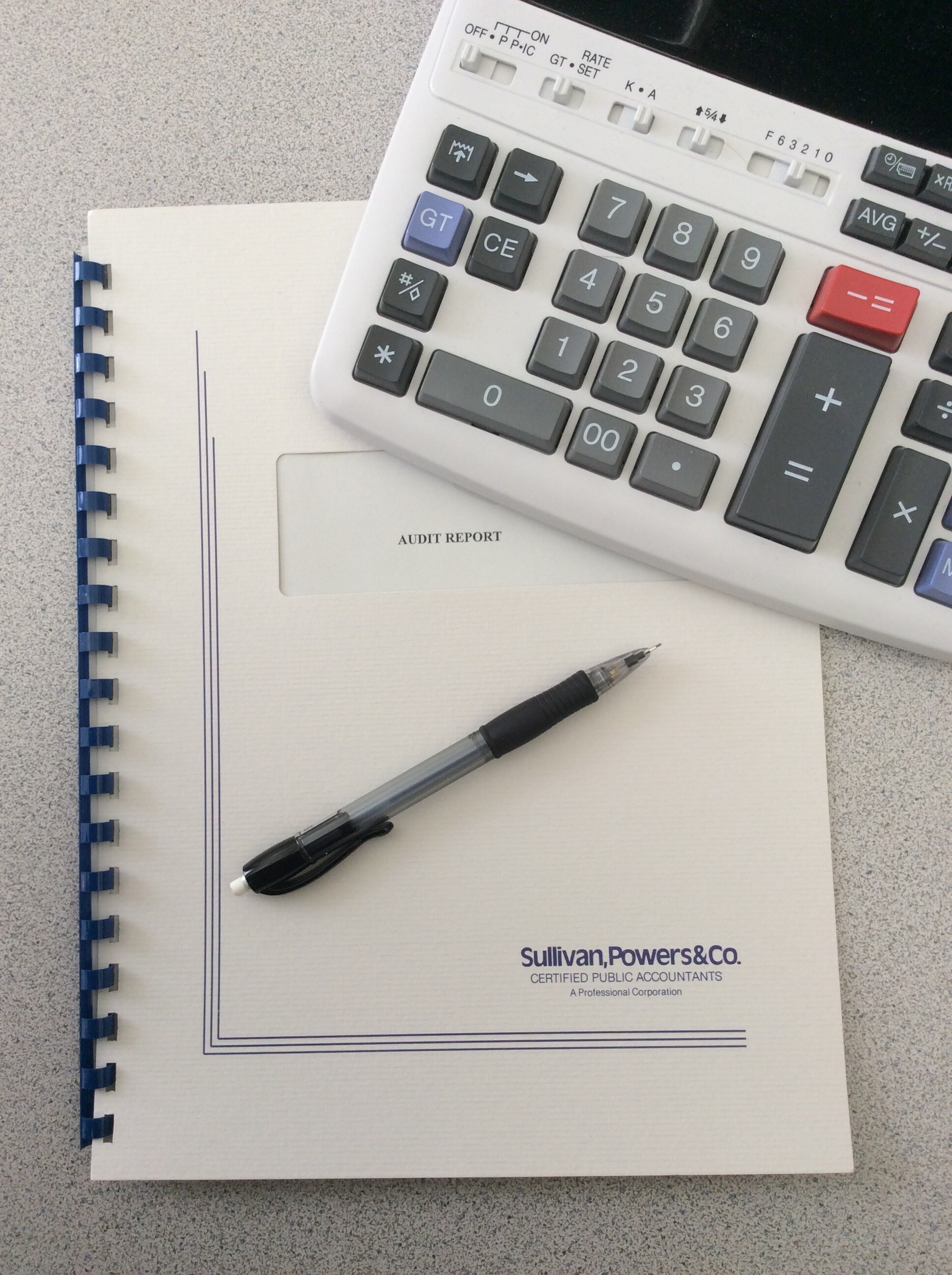 Calculator, pen, and audit report on a grey surface.