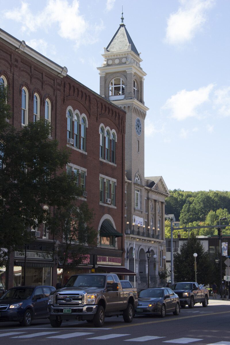 Historic buildings and a clock tower on a bustling street with cars.