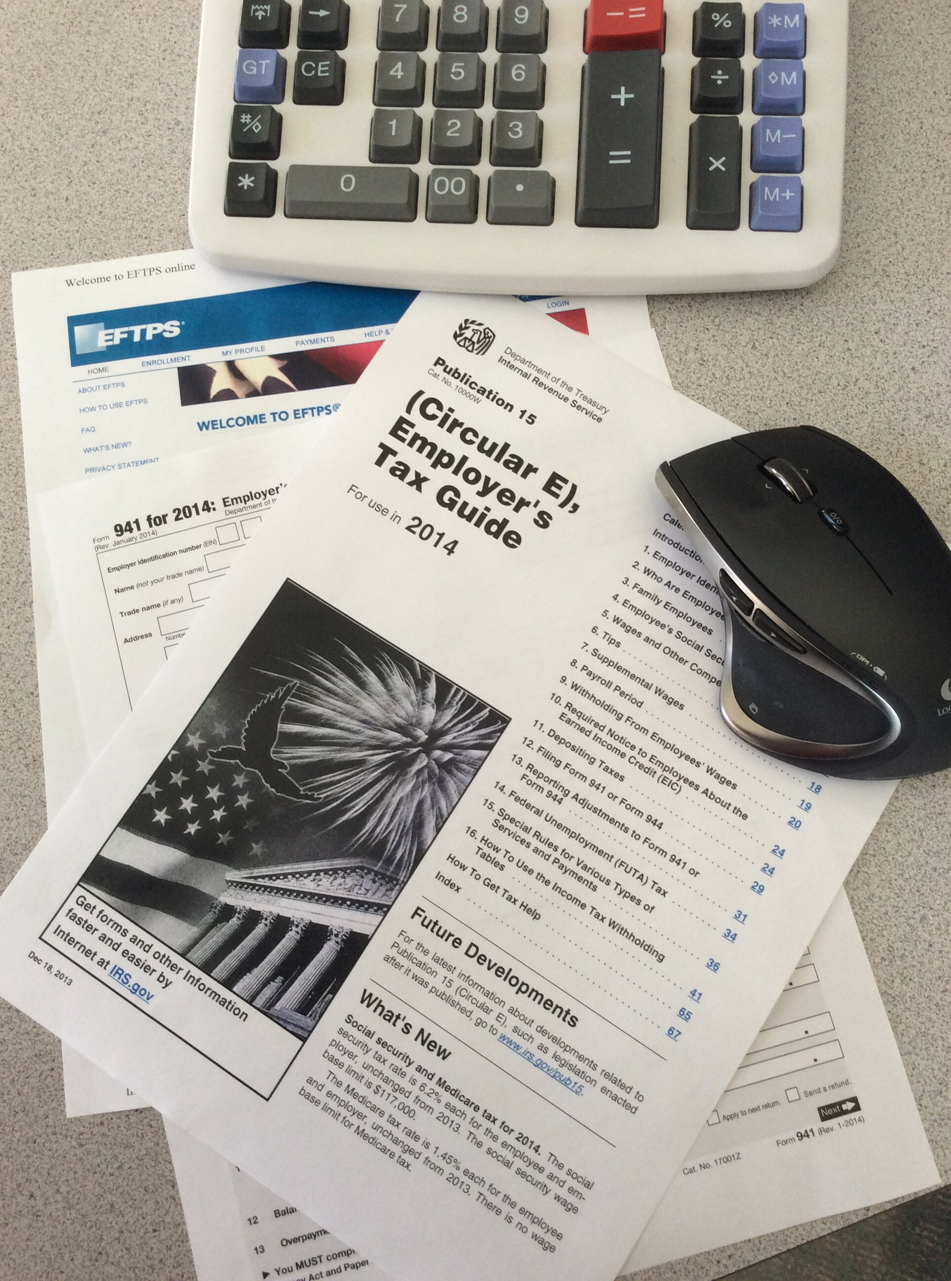 Calculator, mouse, and tax documents on a desk, including an employer's tax guide.