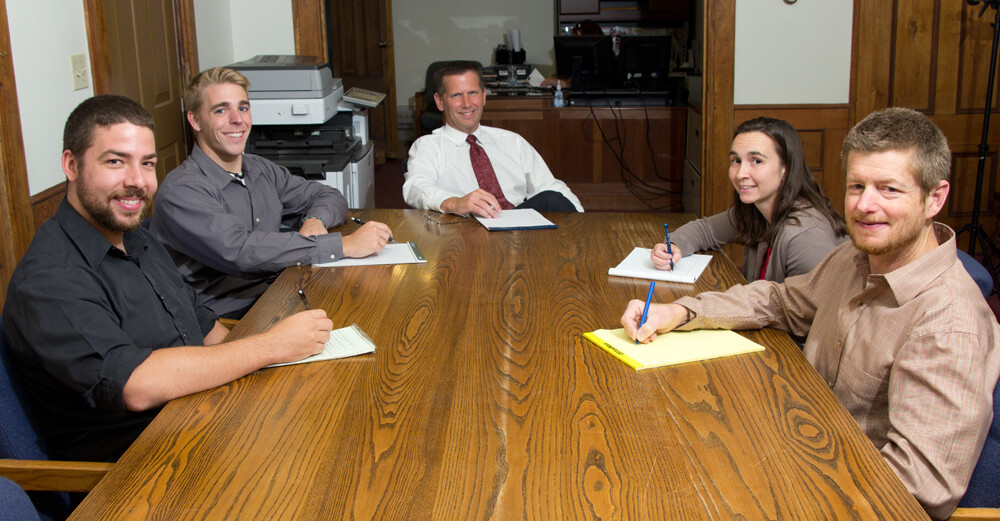 Five people seated at a conference table, taking notes during a meeting.